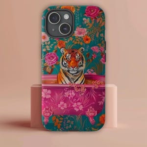 May include: A teal and pink phone case with a tiger in a bathtub surrounded by flowers. The tiger is orange and black with green eyes. The flowers are pink, red, and orange.