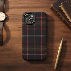 Puede incluir: Funda de teléfono con estampado de cuadros escoceses en azul marino, rojo y dorado. La funda está sobre una superficie de madera, junto a un reloj de cuero marrón y un bolígrafo dorado. La funda tiene un recorte para la cámara.