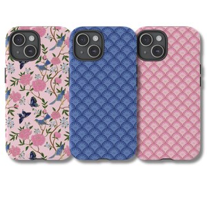 May include: Three phone cases with different designs. The first case is pink with a floral pattern and blue birds. The second case is blue with a geometric pattern. The third case is pink with a geometric pattern.