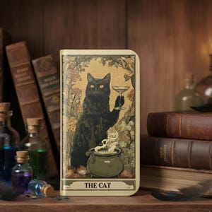 May include: A tarot card-themed phone case featuring a black cat holding a cocktail glass. The cat is depicted in a vintage style, with a cauldron and floral elements. The text "THE CAT" is at the bottom of the case.