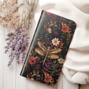May include: A black leather phone case featuring a floral and dragonfly design. The flowers are in shades of red, orange, yellow, and purple. The dragonfly is gold.