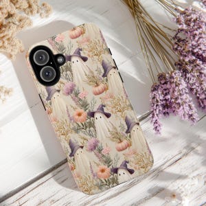 May include: A phone case with a repeating pattern of ghosts in purple witch hats, pumpkins, and floral elements in pastel shades. The design has a vintage, faded look, ideal for Halloween or autumn. The case is designed for a mobile phone.