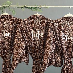May include: Three brown and black leopard print robes with white lettering. The robes are personalized with the names "Joe", "Luke", and "Brian".