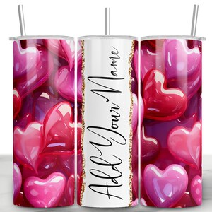 Può includere: Un bicchiere bianco con una striscia di glitter dorata e il testo "Add Your Name" in nero. Il bicchiere è circondato da un motivo di cuori rosa e rossi.