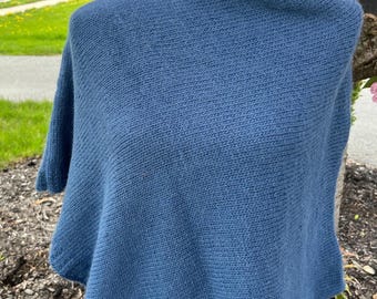 May include: A blue knitted poncho with a loose, drapey fit. The poncho is made of a soft, textured fabric and has a simple, elegant design.