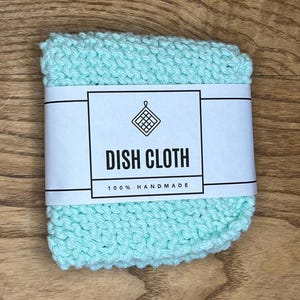 May include: A light blue knitted dishcloth with a white label that says "Dish Cloth 100% Handmade".