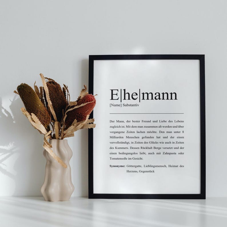 Ehemann Poster in schwarzem Rahmen in modernem Wohnzimmer. Dekoriert mit stilvollem Trockenblumenstrauß in unikater Vase. Zeitloses, personalisierbares Dekor für jeden Wohnraum, perfekt für Liebhaber kreativer Geschenke.