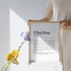 Romantisches Ehefrau Poster im Holzrahmen, gehalten von einer Person. Dekoriert mit Blumen in sanften Tönen. Perfekt als liebevolles Geschenk oder stilvolle Dekoration. Eleganter und femininer Touch.