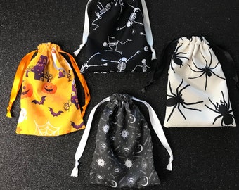 May include: Four Halloween-themed drawstring bags. One bag is black with white skeletons, one is white with black spiders, one is yellow with black bats and orange pumpkins, and one is black with white stars and moons.