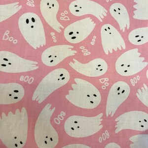 May include: Pink fabric with a repeating pattern of white ghosts with black eyes and mouths. The ghosts have the word "BOO" written on them.