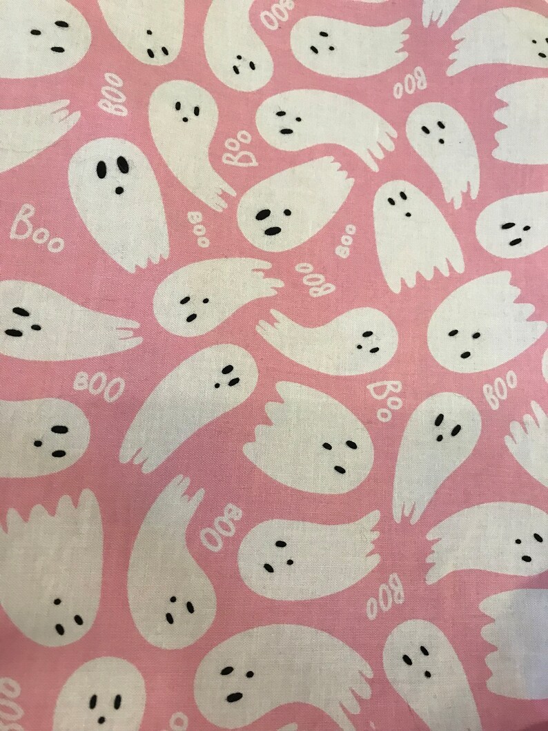 May include: Pink fabric with a repeating pattern of white ghosts with black eyes and mouths. The ghosts have the word "BOO" written on them.