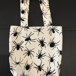 May include: White tote bag with black spider silhouettes printed all over. The bag has two black straps.