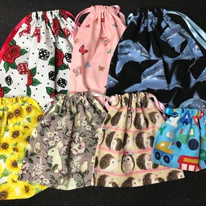 May include: Assortment of 10 colourful drawstring bags with various patterns. The bags feature designs of dice, butterflies, sharks, sunflowers, bunnies, hedgehogs, and trucks.