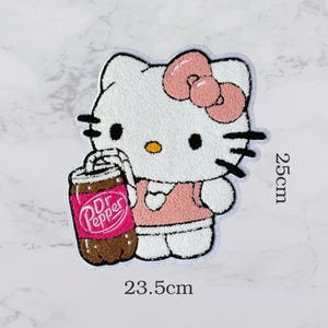 May include: Embroidered patch of a cartoon cat holding a Dr. Pepper drink. The cat is dressed in pink with a matching bow. The patch is 23.5cm wide and 25cm tall.