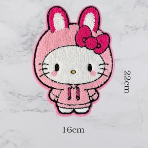 May include: A pink and white cartoon character patch, resembling a cat in a bunny costume, with a pink bow. The patch is 22cm tall and 16cm wide. The character has black eyes, whiskers, and a yellow nose.