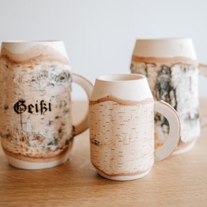 May include: Three birch bark mugs with white handles. The largest mug has the word "Geithi" inscribed on the side.
