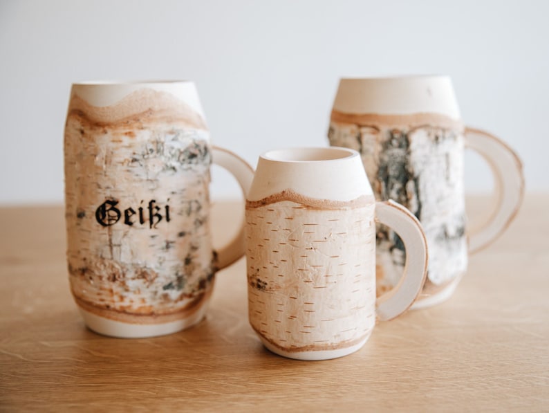 May include: Three birch bark mugs with white handles. The largest mug has the word "Geithi" inscribed on the side.