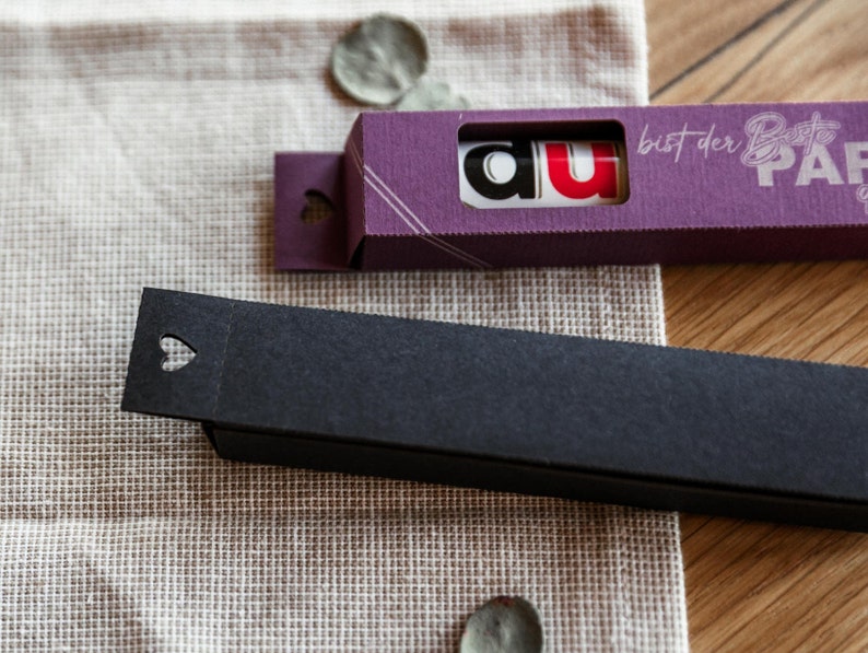 May include: Two small boxes, one purple and one black. The purple box has the text "du" in red and white letters and the text "bist der Beste Papier" in white letters. The black box has a heart-shaped cutout.