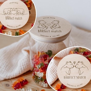 Könnte beinhalten: Ein klares Glas mit einem Holzdeckel mit der Aufschrift "BÄRfect match" und den Namen "Marina & Julian". Der Deckel hat eine Illustration von zwei Bären. Das Glas ist mit bunten Gummibärchen gefüllt.