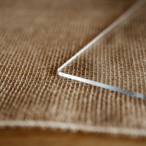 Op de afbeelding: Een close-up van een doorzichtig acrylplaat dat op een bruine jute ondergrond ligt.