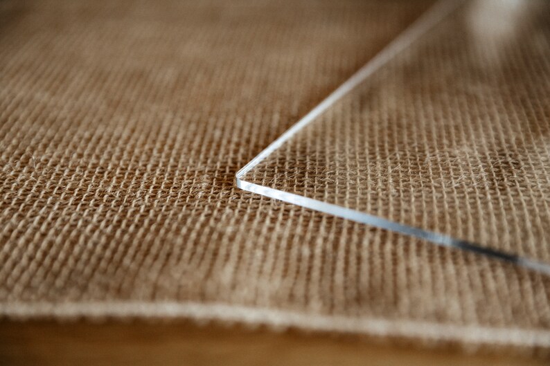 Op de afbeelding: Een close-up van een doorzichtig acrylplaat dat op een bruine jute ondergrond ligt.