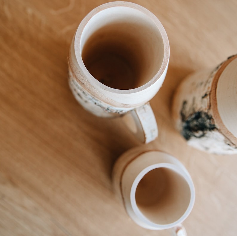 May include: Three wooden mugs with a natural birch bark design. The mugs are all different sizes and have a natural wood finish.