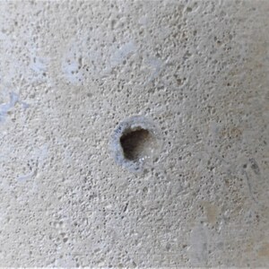K&ouml;nnte beinhalten: Nahaufnahme einer hellgrauen Betonfl&auml;che mit einem kleinen, quadratischen Loch in der Mitte.