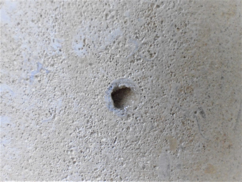 K&ouml;nnte beinhalten: Nahaufnahme einer hellgrauen Betonfl&auml;che mit einem kleinen, quadratischen Loch in der Mitte.