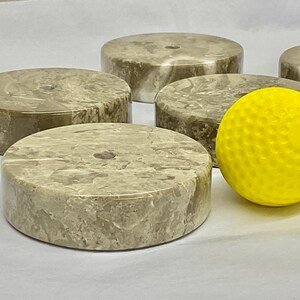 May include: Five round, light brown marble coasters with a yellow golf ball in the centre.