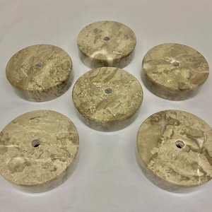 May include: Six round, beige marble bases with a hole in the centre. The bases are all different sizes and have a natural, marbled pattern.