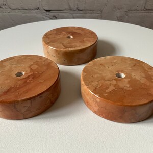 May include: Three round, brown marble bases with a hole in the centre. The bases are different sizes and have a mottled pattern.
