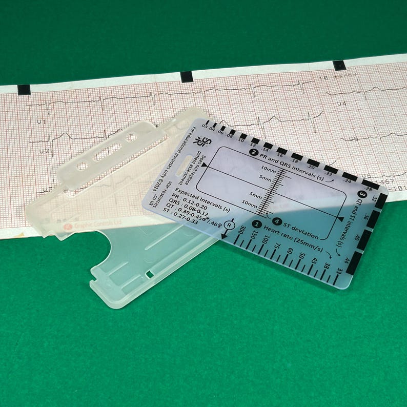 May include: A clear plastic ruler with markings for measuring heart rate, ST deviation, and PR and QRS intervals in seconds. The ruler is labeled with expected intervals for PR, QRS, QT, and ST segments. The ruler is on a green surface.