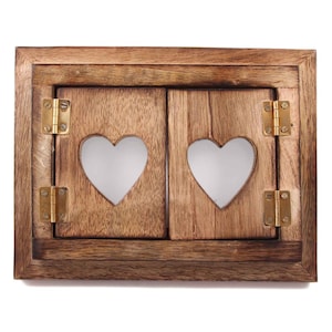Puede incluir: Un marco de ventana de madera con dos contraventanas, cada una con un recorte en forma de corazón. Las contraventanas están cerradas y tienen bisagras de latón.