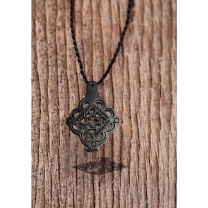 May include: Black pendant necklace with an ornate, symmetrical design. The pendant is suspended from a black cord and is set against a wooden background. The text "front side" is visible below the pendant.