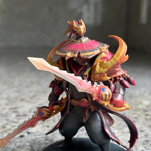 May include: A red and gold painted figurine of a warrior holding a sword. The warrior is wearing a red and gold helmet and armor. The figurine is standing on a black base.