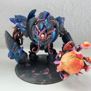Può includere: Una miniatura stampata in 3D di una creatura blu scuro e viola con un occhio arancione luminoso. La creatura tiene un globo arancione luminoso nella sua mano destra. La miniatura è in piedi su una base nera.