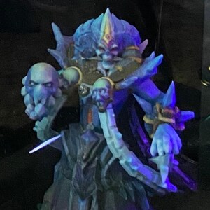 May include: A blue and purple fantasy figurine of a creature with a skull in each hand. The creature has a crown and a long flowing robe.