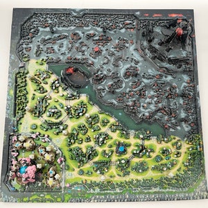 May include: A 3D printed game board with a green and brown landscape on one side and a black and gray landscape on the other side. The board is divided into two sections by a river.