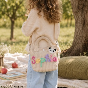 May include: A beige corduroy handbag featuring a top handle and a detachable shoulder strap. The bag is decorated with a plush panda face patch and the name Sophia spelled out in colorful, textured yarn letters across the front surface.