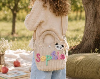 May include: A beige corduroy handbag featuring a top handle and a detachable shoulder strap. The bag is decorated with a plush panda face patch and the name Sophia spelled out in colorful, textured yarn letters across the front surface.