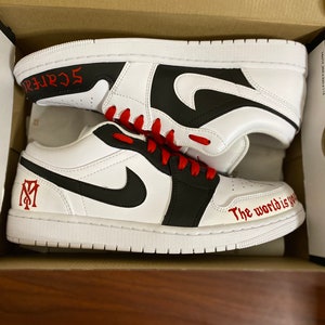 May include: A pair of white and black sneakers with red laces. The left shoe has a red "M" logo and the right shoe has the text "The world is yours" written in red.