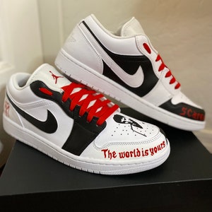 May include: White and black low-top sneakers with red laces. The right shoe has the text "The world is yours" written on the side. The left shoe has the text "5 Cars" written on the side.