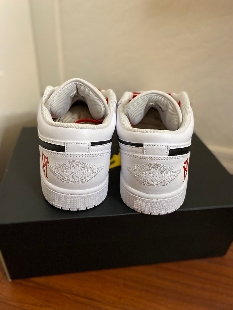May include: A pair of white leather low-top sneakers with black accents and red stitching. The sneakers have a white midsole and a black outsole. The Jordan logo is visible on the tongue and the back of the shoe.