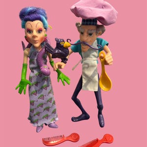 Peut inclure: Deux poupées vintage : une femme aux cheveux violets et une robe à imprimé raisin, et un chef avec un chapeau rose et une moustache. Comprend deux peignes rouges et un oiseau violet. Sur fond rose.