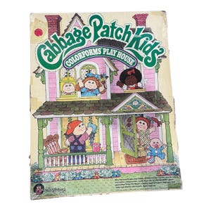 May include: A Cabbage Patch Kids Colorforms Play House toy box featuring a two-storey illustrated house with green trim, a porch, and various Cabbage Patch Kids characters. The box displays the brand name in large green text and includes small text.