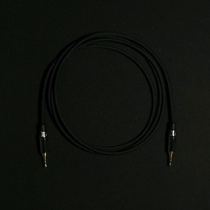 Könnte beinhalten: Ein schwarzes Audiokabel mit vergoldeten Steckern. Das Kabel ist aufgerollt und hat eine geflochtene Außenhülle.