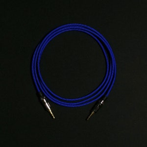 Könnte beinhalten: Ein blaues geflochtenes Audiokabel mit vergoldeten Steckern. Das Kabel ist zu einem Kreis gewickelt.