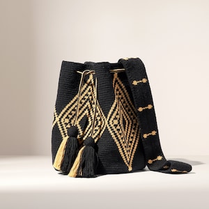 May include: Black and gold woven bucket bag with a geometric diamond pattern. The bag has a drawstring closure, a long shoulder strap, and tassels. The bag is made of a woven material.