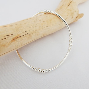 Peut inclure: Un bracelet jonc en argent avec une rangée de petites perles argentées.