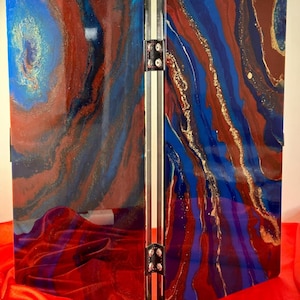 May include: A two-panel room divider with a blue, red, and gold abstract design. The panels are hinged together and have a metallic finish.